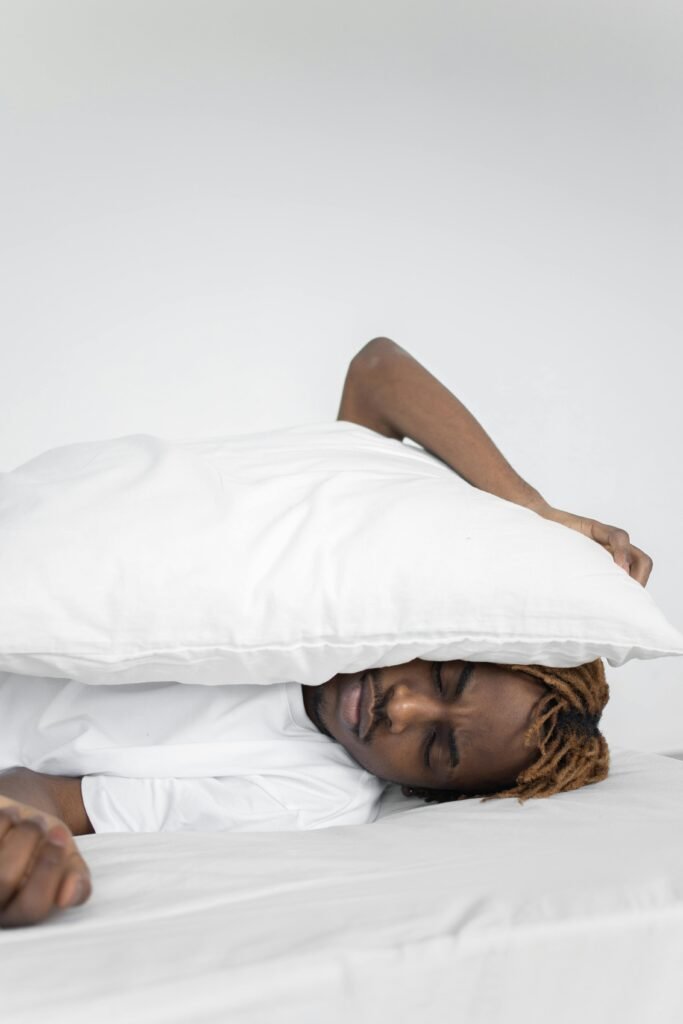 Ndukaku Fitness Serene image of a young adult black man peacefully sleeping with a white pillow under soft lighting.